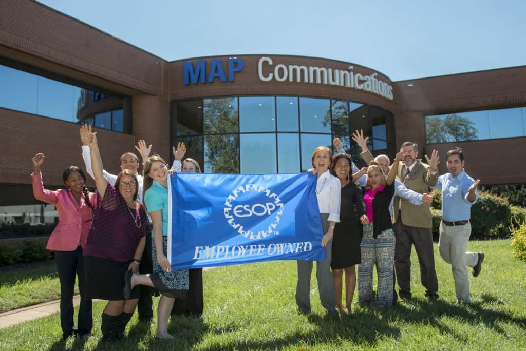 Image of MAP team members holding a flag that says we are an employee owned company in front of our headquarters