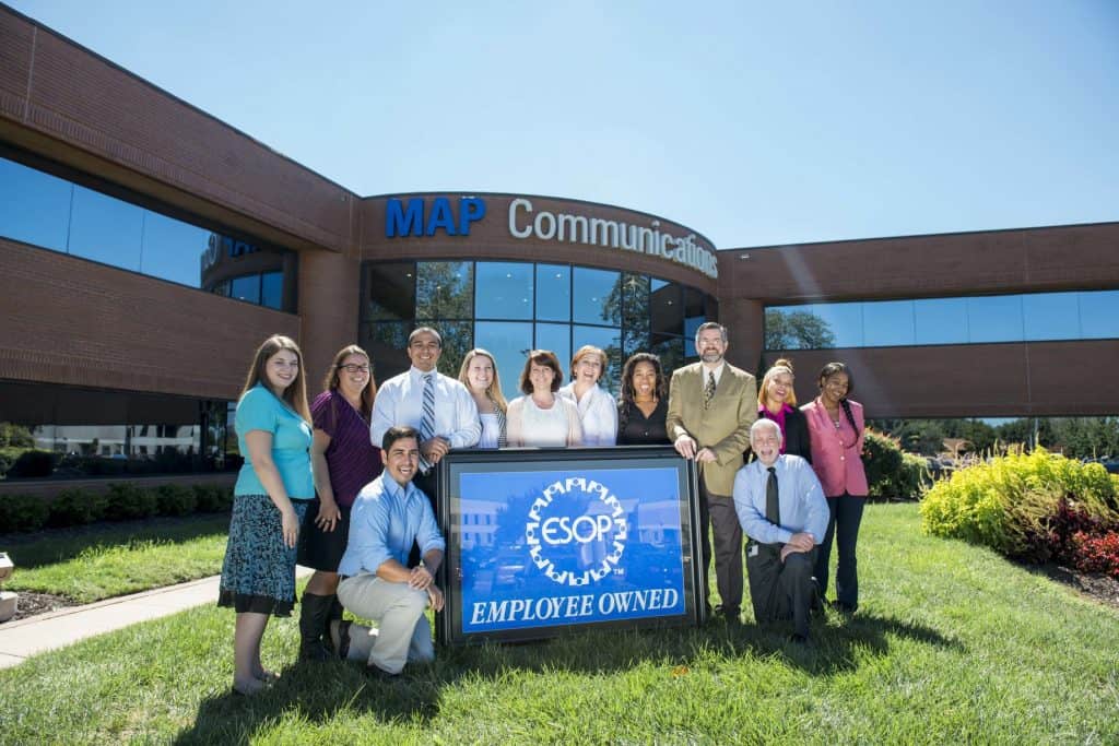 Image of MAP Communications team members holding a sign that says we are an employee owned company in front of our headquarters