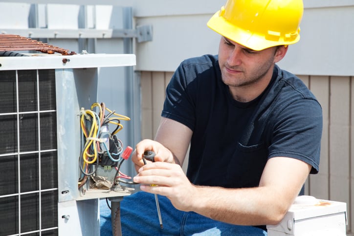 Image of a contractor working on an air conditioner who uses an HVAC Answering Service
