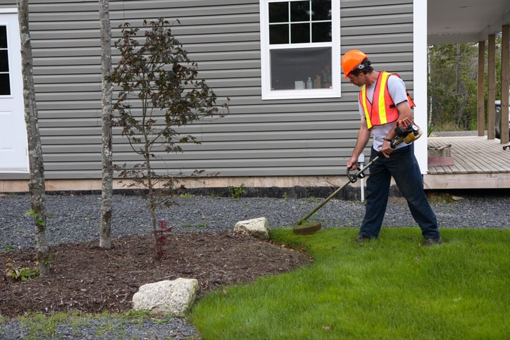 Image of a man trimming a lawn who uses a landscaping answering service