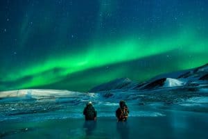 Image of a snowy landscape with two people looking at the Aurora Borealis